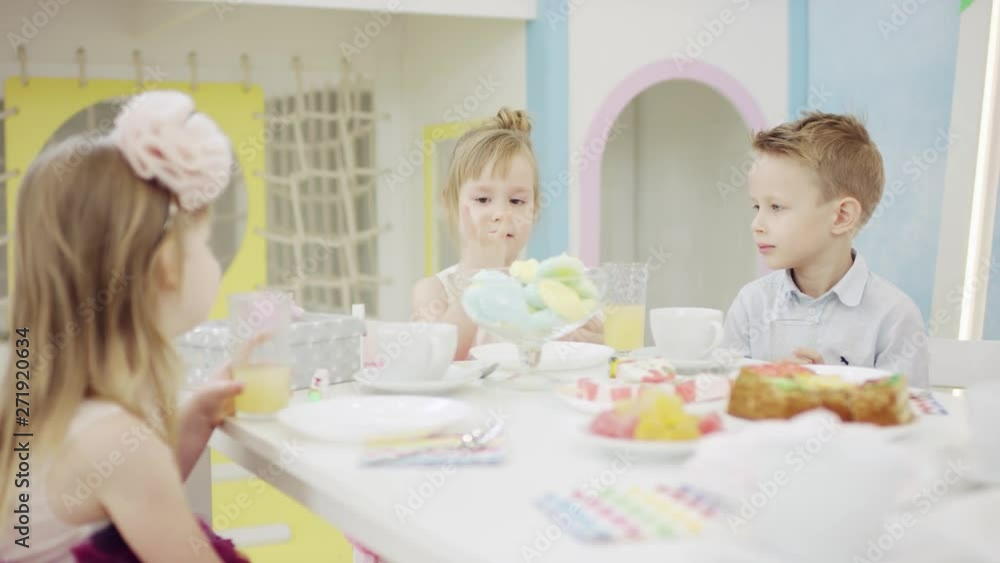 Adult woman sitting by table and talking with children on a kids party Adult woman sitting by table and talking with children on a kids party