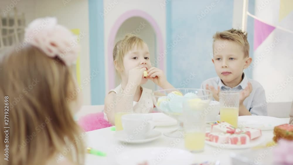 Adorable children sitting by table and eating marshmallow Adorable children sitting by table and eating marshmallow