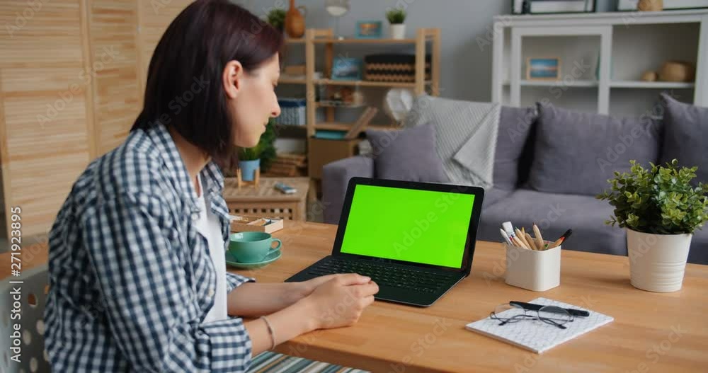 Student young lady is watching laptop with green screen smiling sitting at desk in apartment enjoying movie in the internet. People, entertainment and gadgets concept. Student young lady is watching laptop with green screen smiling sitting at desk in apartment enjoying movie in the internet. People, entertainment and gadgets concept.