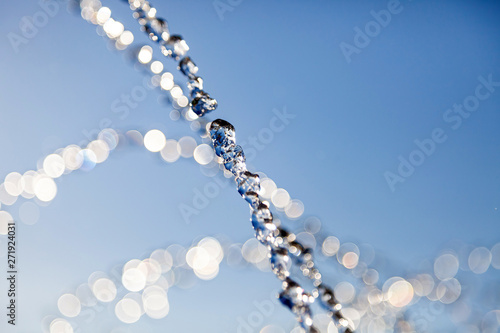 Water droplets frozen in the air with splashes and chain bubbles on a blue isolated background in nature. Clear and transparent liquid symbolizing health and nature.