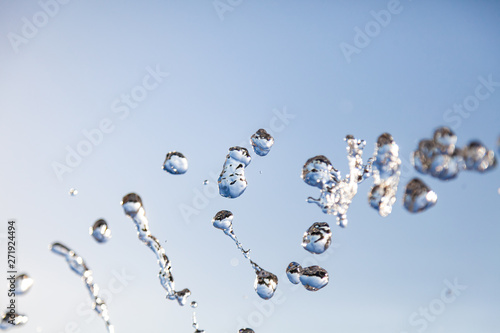 Water droplets frozen in the air with splashes and chain bubbles on a blue isolated background in nature. Clear and transparent liquid symbolizing health and nature.