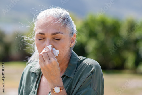 Senior woman blowing nose in napkin