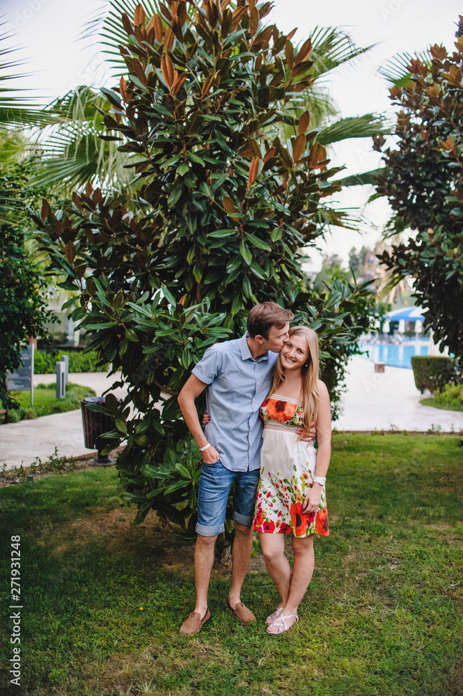Loving young couple hugging and standing at the palm bush in the park. Kiss. Against the background of the pool. Honeymoon. Vacation. Turkey. Close up