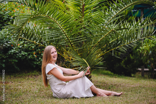 Beautiful  young  slender  long-haired blond girl in white long dress against the backdrop of palm trees and nature. Turkey. Model stylish. Fashion. Smiles. Happy. close up