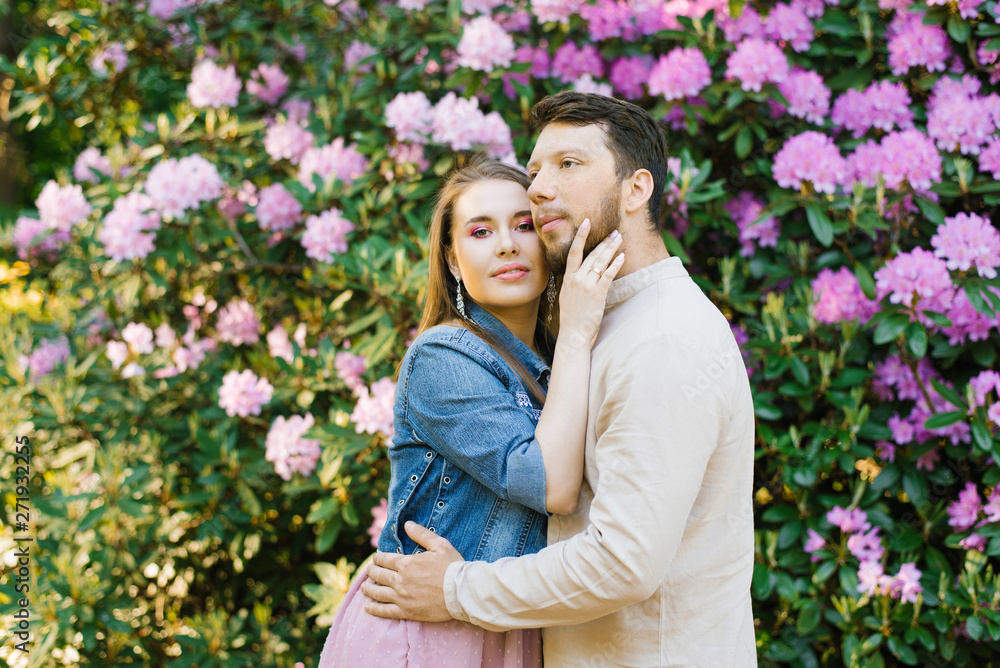 the guy hugs the girl on the background of rhododendron flowers. girl looks into the camera. tenderness and happiness in relationships the guy hugs the girl on the background of rhododendron flowers. girl looks into the camera. tenderness and happiness in relationships