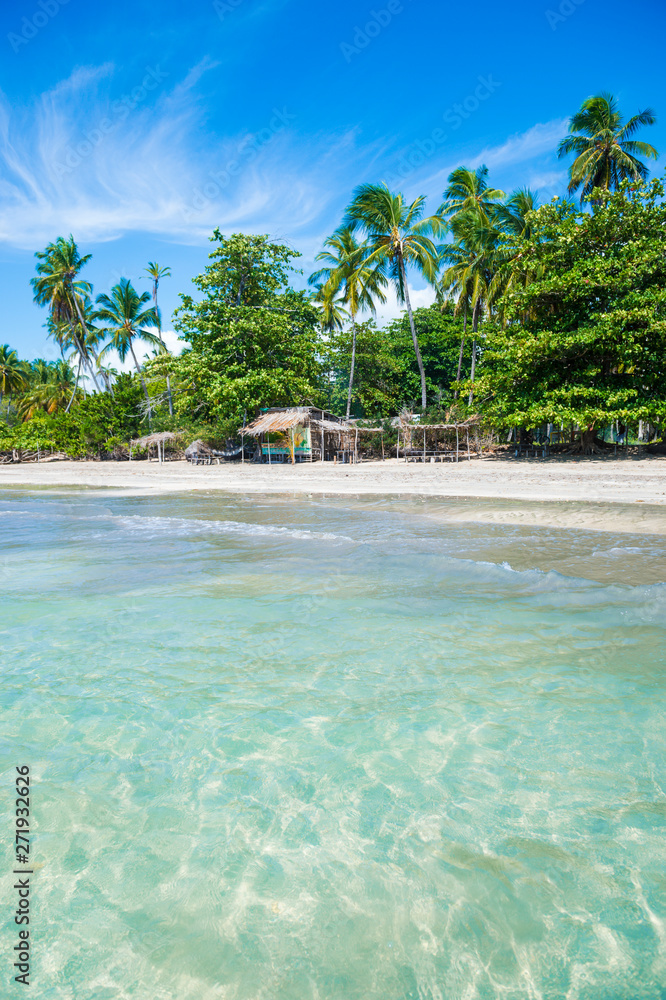 Obraz premium Bright sunny view of empty beach lined with rustic wooden beach shacks on the coast of a remote island in Bahia, Brazil