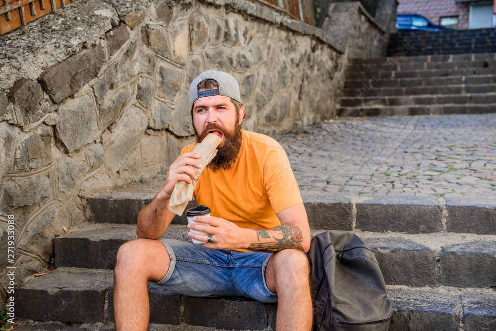 Meal just tastes better out. Hipster eating hot dog meal on stairs outdoor. Caucasian guy enjoy eating takeaway meal. Bearded man eating unhealthy hotdog sandwich during rest and meal break