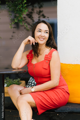 beautiful smiling middle-aged brunette in a red dress sitting at a table of a street cafe