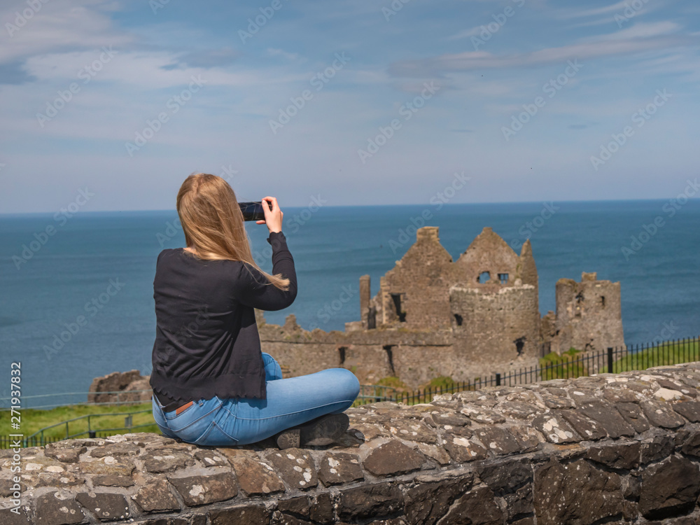 Young woman takes photos of Dunluce Castle in North Ireland - travel photography