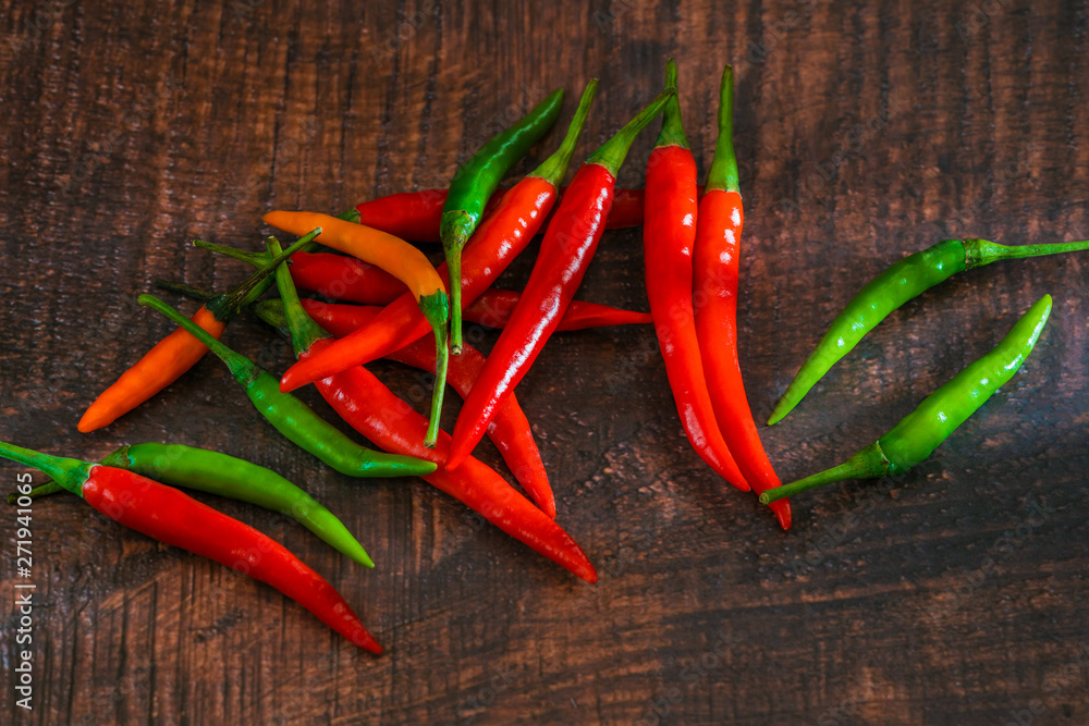 Red, green and orange chili peppers on wooden background