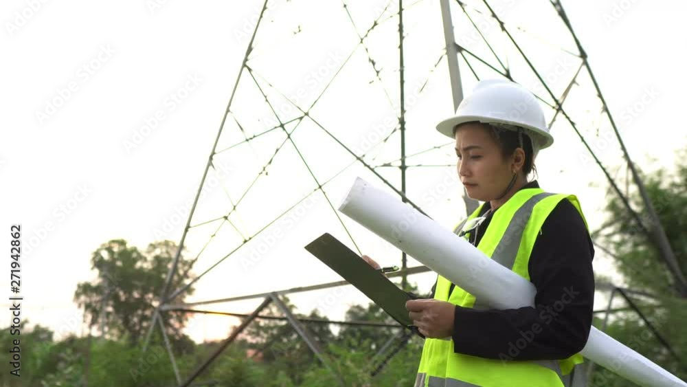 Asian senior electrical engineer working at site of big pole high voltage on sunset Asian senior electrical engineer working at site of big pole high voltage on sunset