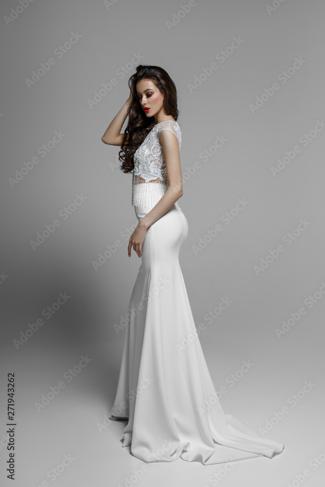 Image from side view of a sexy brunette model in classic white wedding dress, on white background.