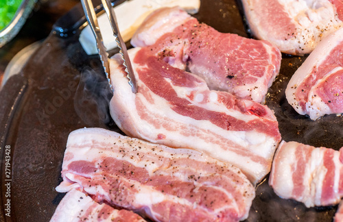 Black pork raw meat on iron pan in Korea restaurant, fresh delicious korean food cuisine on iron plate with lettuce, close up, copy space, lifestyle