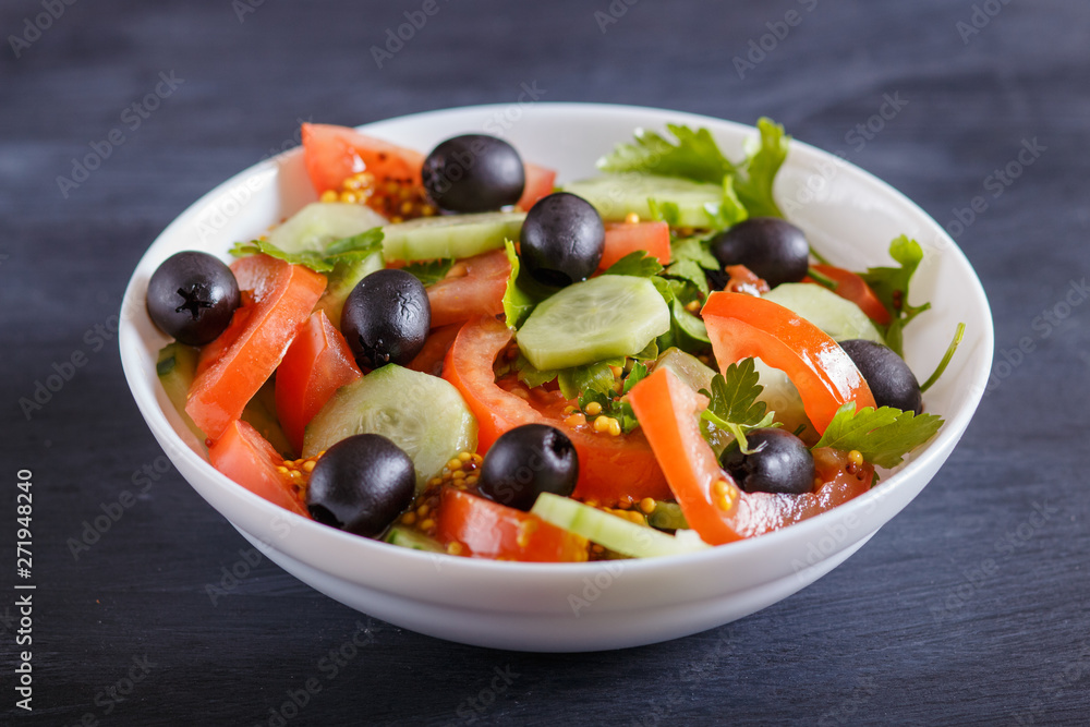Vegetarian salad of tomatoes, cucumbers, parsley, olives and mustard on black wooden background.