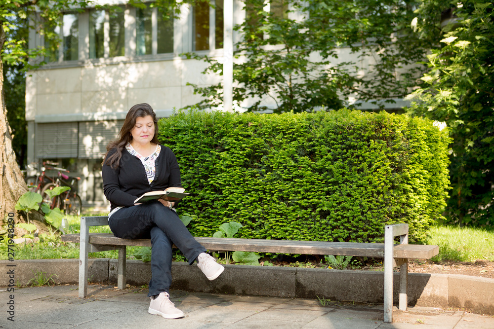 Fototapeta premium Lady Sitting on City Bench while Reading a Book
