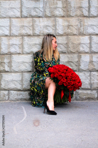 a girl in a green dress with a bouquet of red roses at the concrete wall