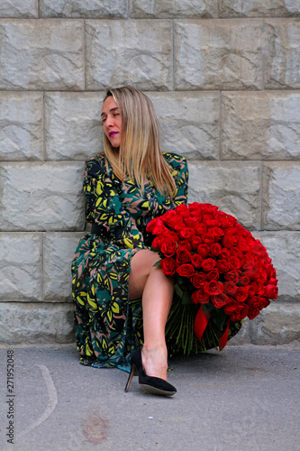 a girl in a green dress with a bouquet of red roses at the concrete wall