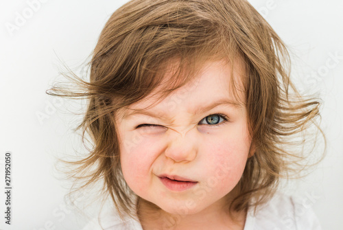 Happy funny baby eyewink isolated on white background. Beautiful close portrait of a girl winking with blue eyes photo