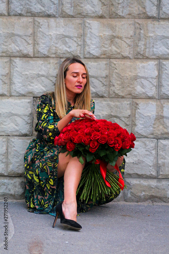 a girl in a green dress with a bouquet of red roses at the concrete wall