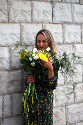 a girl in a green dress with a bouquet of yellow flowers at the concrete wall