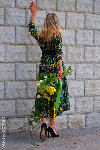 a girl in a green dress with a bouquet of yellow flowers at the concrete wall