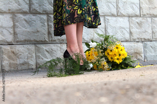 a girl in a green dress with a bouquet of yellow flowers at the concrete wall