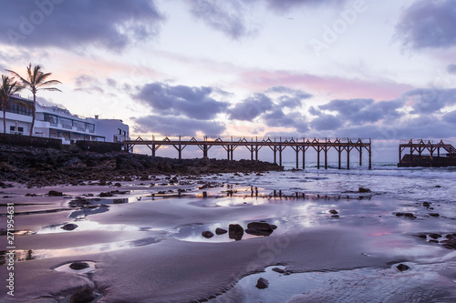 Bridge on the beach at sunset. Cloudy sky and palm tree.