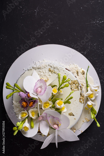 Chocolate cake decorated with flowers and poured white icing on black stone background. Top view. Flat lay. photo