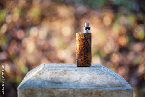 high end natural stabilized wood box mods with rebuildable dripping atomizer on bokeh texture background, vaping device, selective focus photo