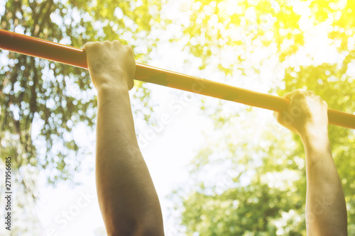 Foto the hands of a sports athlete hold on to a metal crossbar for pull-ups on the training ground against a clear sky and green foliage