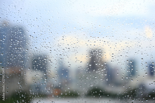 office window covered with rain water. water spray on window. after rain traffic, worker stuck in the office concepts. blur urban skyline background. rainy season concepts. © suebsiri