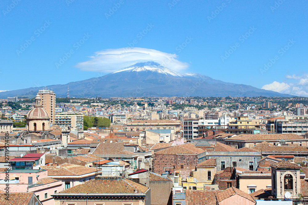 Majestic Mount Etna overlooking the Sicilian city Catania, Italy. Smoke cloud over the famous volcano, snow on the top. Dominant of the cityscape is the cupola of Catania Cathedral of Saint Agatha
