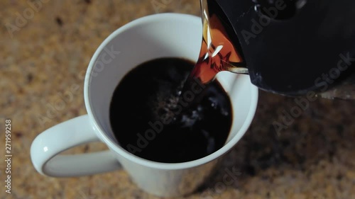Coffee pot pouring fresh home brewed coffee into white cup.