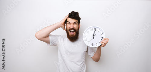 Portrait of a bearded man holding clock, delay and worried about discipline photo