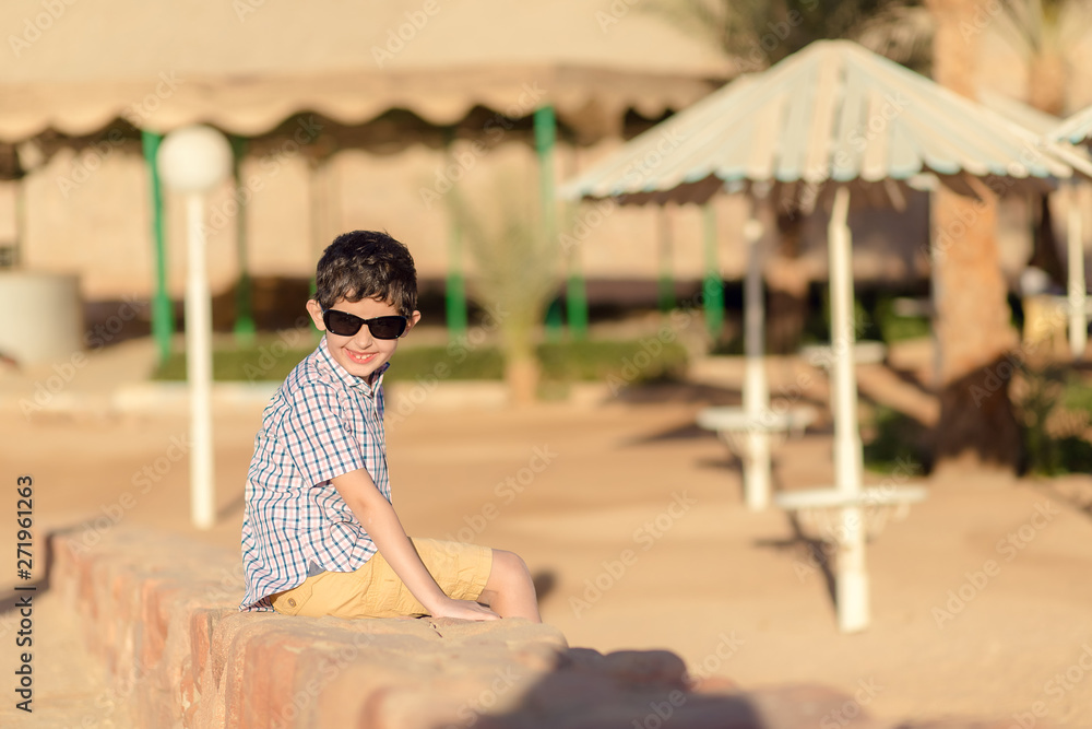 Boy in a shirt is sitting on the beach