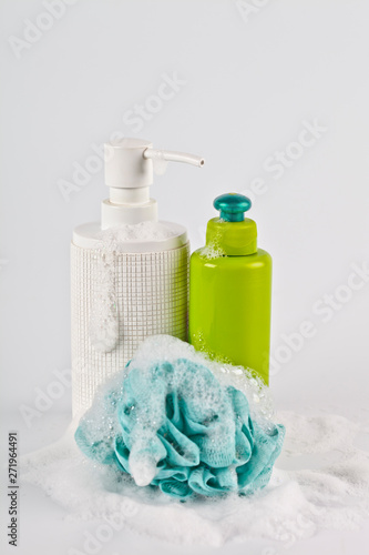 Bath cosmetic products, green sponge and foam on light background.