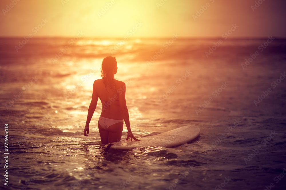 Attractive woman standing in ocean with surfboard