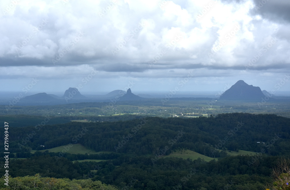 Obraz premium Panoramic view of Glass House Mountains National Park on Sunshine Coast (Queensland, Australia). The Glasshouse Mountains are silhouetted in the afternoon sunlight.
