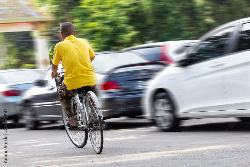 Fototapeta premium Asian men wear yellow shirts, biking with cars running as blurred images in the background. Concept of transportation and Inequality.