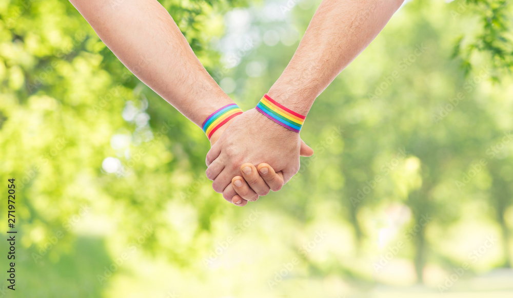lgbt, same-sex relationships and homosexual concept - close up of male couple wearing gay pride rainbow awareness wristbands holding hands over green natural background lgbt, same-sex relationships and homosexual concept - close up of male couple wearing gay pride rainbow awareness wristbands holding hands over green natural background