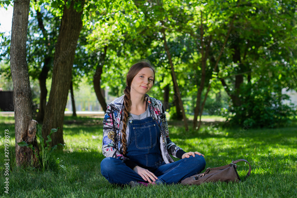 beautiful woman in denim overall sitting on the green grass in the Park beautiful woman in denim overall sitting on the green grass in the Park