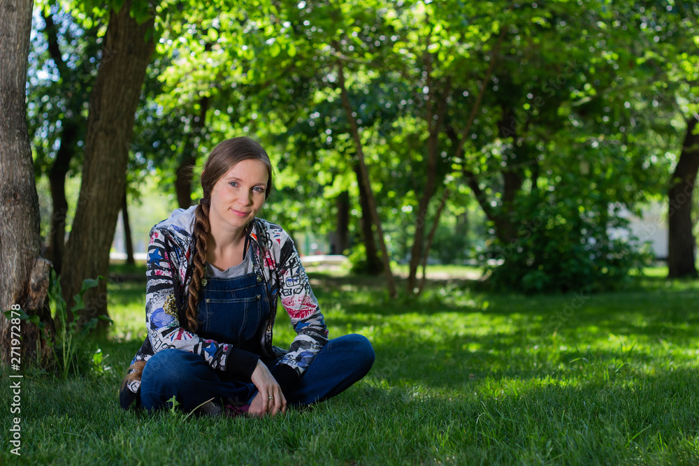 beautiful woman in denim overall sitting on the green grass in the Park beautiful woman in denim overall sitting on the green grass in the Park
