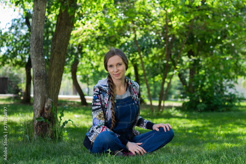 beautiful woman in denim jumpsuit sitting on the green grass in the Park beautiful woman in denim jumpsuit sitting on the green grass in the Park
