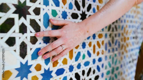 Closeup of a hand brushing along ornate colorful mosaic tile pattern on a wall
