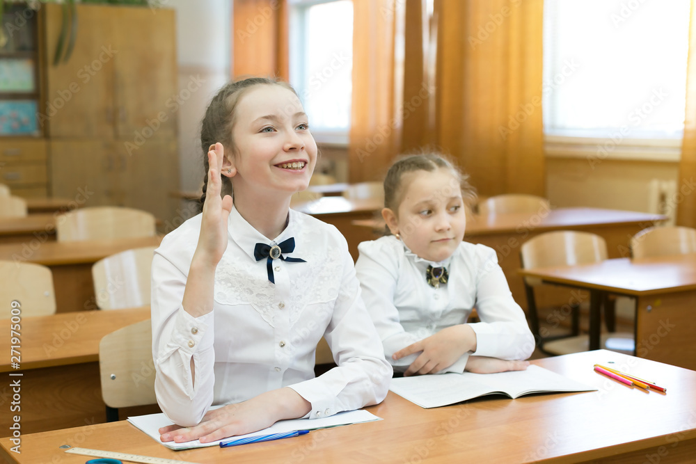 Children sit in school, one raises his hand. schoolgirl girl raises her hand to answer the teacher's question, the second girl does not know the answer. Children sit in school, one raises his hand. schoolgirl girl raises her hand to answer the teacher's question, the second girl does not know the answer.
