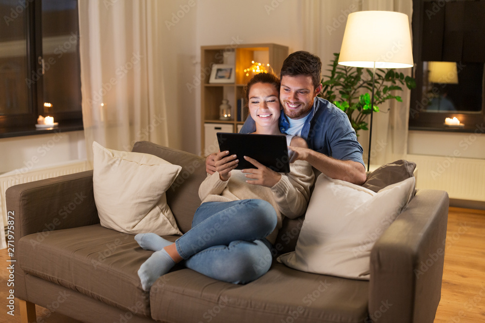 Obraz premium technology, internet and people concept - happy couple using tablet computer at home in evening