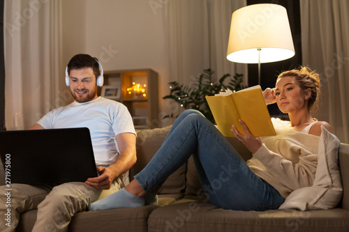 leisure and people concept - couple with laptop computer and book at home in evening photo