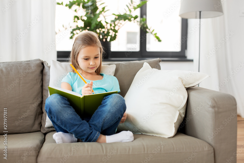 people, childhood and bedtime concept - little girl with diary and pencil sitting on sofa at home