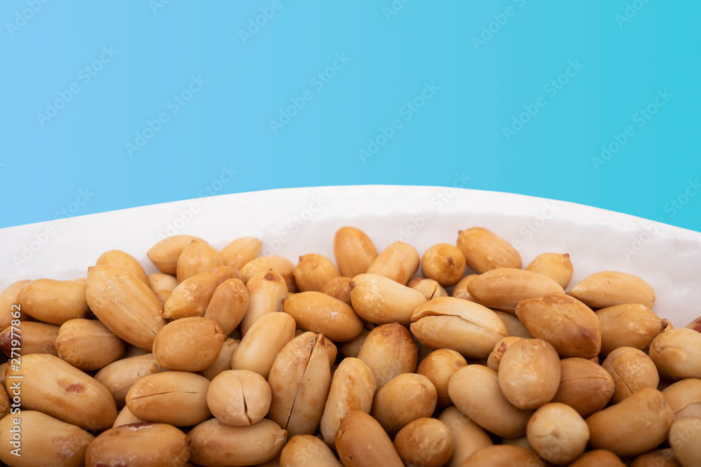 Roasted peanuts in bowl, heap of peanut on blue background, closeup photo Roasted peanuts in bowl, heap of peanut on blue background, closeup photo