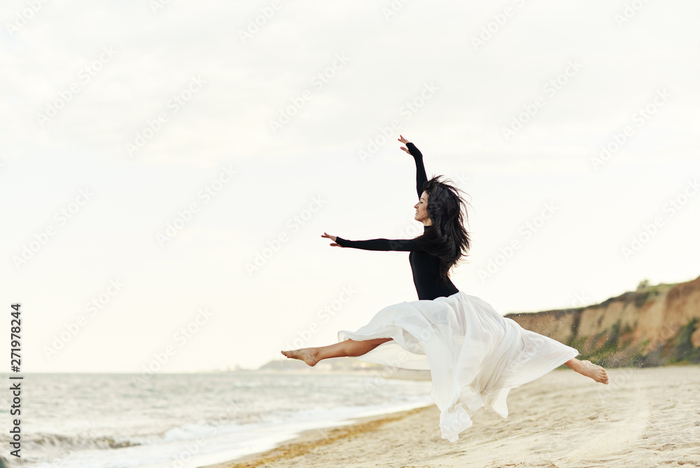 Classical dancer woman. Charming ballerina with windy hair in white chiffon skirt dancing by the sea background. Sun shines on her. Classical dancer woman. Charming ballerina with windy hair in white chiffon skirt dancing by the sea background. Sun shines on her.